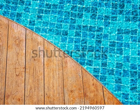 Top view of empty wooden plank table or deck floor curved shape in front of the blurred background of blue mosaic tiles grid pattern in swimming pool. Empty space on poolside, summer background. Royalty-Free Stock Photo #2194960597