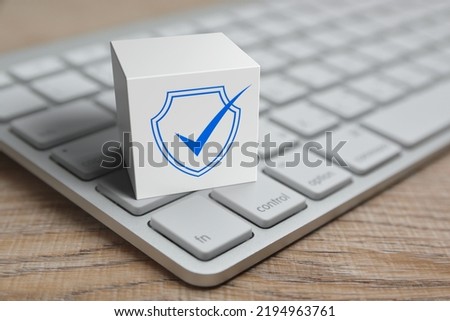 Security shield with check mark flat icon on white block cube with modern computer keyboard on wooden table, Technology internet cyber security and anti virus online concept