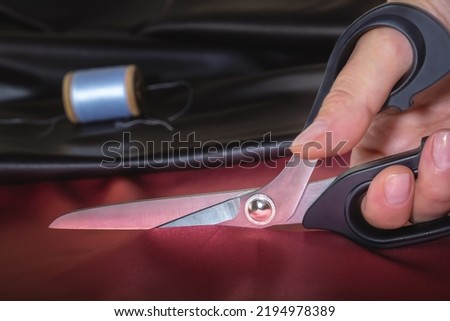 Tailor's scissors in a woman's hand cut the fabric. Close-up