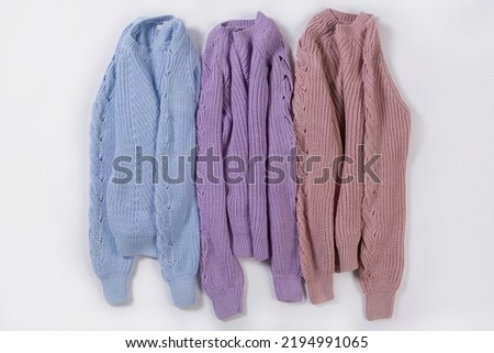 Three knitted sweaters in pastel colors, lying side by side on a white background, concept
