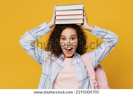Young smiling happy fun smart black teen girl student she wear casual clothes backpack bag hold pile of books on head isolated on plain yellow color background. High school university college concept