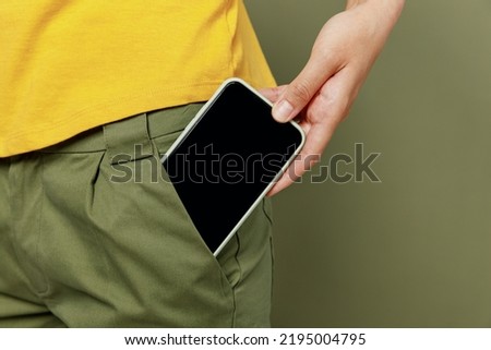 Close up cropped photo shot woman she wear yellow t-shirt holding in hand put into pants pocket mobile cell phone with blank screen workspace area card isolated on plain olive green khaki background. Royalty-Free Stock Photo #2195004795