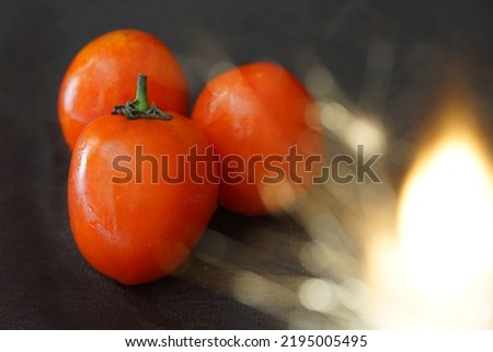 Picture of three tomatoes with fire flare on a black background.                         