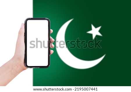 Close-up of male hand holding smartphone with blank on screen, on background of blurred flag of Pakistan.
