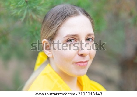 An inclusive portrait of a young smiling woman in yellow clothes against the backdrop of a coniferous forest and pine needles. Chubby cheeks, potato nose. Royalty-Free Stock Photo #2195013143