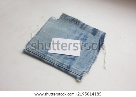 A blank business name card is on blue grunge denim texture fabric, isolated on white background, for stylish identity branding mockup or fashion designer portfolio presentation.