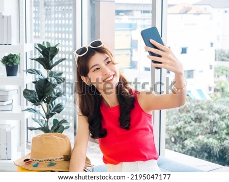 Young beautiful smiling Asian woman holding smart mobile phone and make selfie by camera. Happy Asian female wearing sunglasses and beach hat, take a lively portrait photo, travel summer vacation.