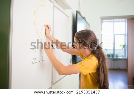 student draws triangle on blackboard in school classroom. teenager child measures angle with protractor in math geometry lesson in middle link.