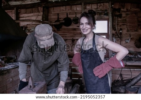 Smiling woman in a leather work apron and large mittens in an old forge