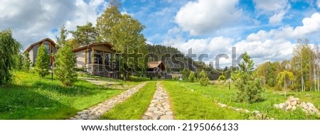 Modern village. Real estate in ecologically clean place. Panorama with rural town houses. Wooden cottages at foot hill. Summer landscape ECO village. Stone path leads to summer houses. ECO property Royalty-Free Stock Photo #2195066133