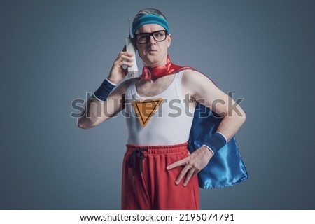 Superhero making a phone call using an old obsolete cordless telephone, he is making a funny expression