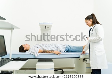 Female radiologist starting the densitometry machine scan to perform a medical exam and check the bone density of a sick woman