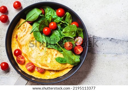 Omelet with fresh spinach and tomato salad in a frying pan on a gray table, top view. Breakfast food. Royalty-Free Stock Photo #2195113377