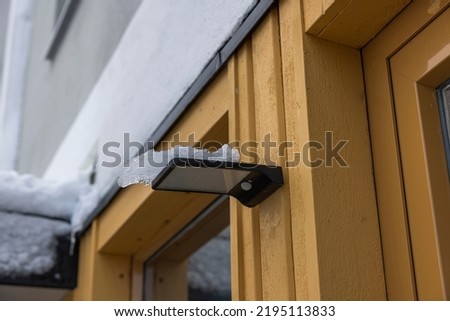 Close up view of wooden villa with outdoor lamp with solar panel and motion sensor covered in snow. Sweden. Royalty-Free Stock Photo #2195113833