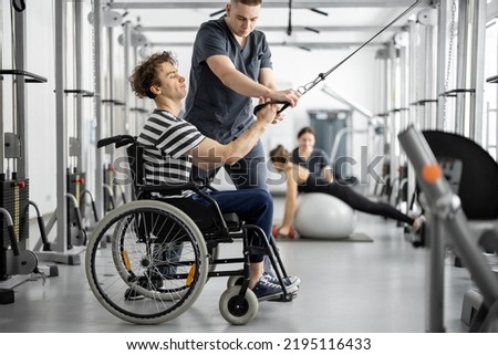 Rehabilitation specialist helps a guy in a wheelchair to do exercise on decompression simulator for recovery from injury Royalty-Free Stock Photo #2195116433