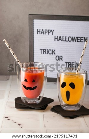 Decorating a Halloween party with your own hands. Halloween drinks. Pumpkin cocktail with orange, tomato juice in glass glasses decorated with scary faces on a white table. selective focus.