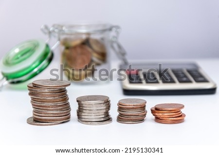 Metal coins in stacks, a calculator for counting money, a jar with small coins on a white background, close-up, selective focus.Concept: financial savings, expenses and income.