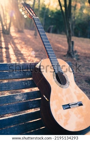 Beautiful classical guitar on a bench in the park with lens flare. Photo of a new wooden guitar with nylon strings outdoors in the summer during sunset. No people. Beautiful string instrument. Royalty-Free Stock Photo #2195134293