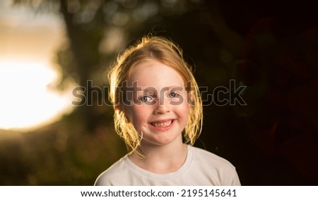 Young Caucasian female smiling and looking into camera with the sun on her back outdoors.