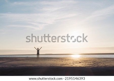 child with arms raised up against the background of the sky,sand on the beach at sunset. Silhouette of a boy at sunset. Beautiful landscape, on the right there is a place for an inscription