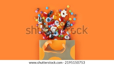 Shopping paper orange polka dot gift bag full of spilled assorted traditional Halloween candies. Orange banner background with copy space. Happy Halloween holiday sale and trick or treat concept.