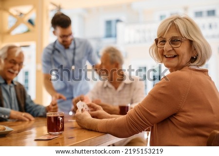 Happy mature woman enjoying in playing card with her friends on patio at residential care home. Royalty-Free Stock Photo #2195153219