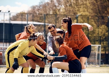 Cheerful female soccer players and their coach gathering hands in unity before the match on playing field. Royalty-Free Stock Photo #2195154465