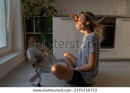 Exhausted young woman refreshing sit near big indoor ventilator blowing cooling fresh air at home on floor bonding. Tired female enjoying conditioner having fun indoors. Summer, heat weather concept Royalty-Free Stock Photo #2195158733