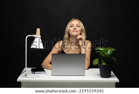 Portrait of attractive happy freelancer woman in a black t-shirt with a laptop in a studio with a black wall.