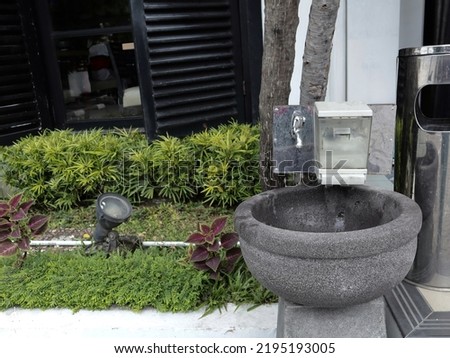 a hand washing place made of black stone which is on the edge of a mini garden