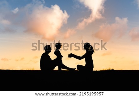 Silhouette of happy family sitting in the park in nature sunset. 