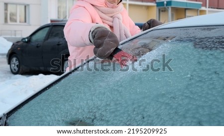 Woman is Cleaning a Windshield of her Car with Ice Scraper, Winter Driving Royalty-Free Stock Photo #2195209925