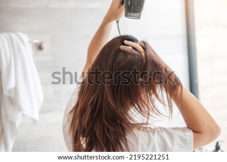 young woman using hair dryer at home or hotel. Hairstyles and lifestyle concepts Royalty-Free Stock Photo #2195221251