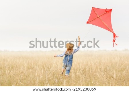 Little girl runs outdoors. Cheerful and happy child plays and launches a kite in the field against the blue sky. Kid dreams of flying and aviation. Royalty-Free Stock Photo #2195230059