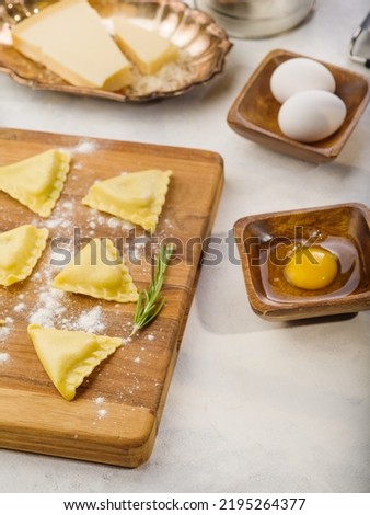 Homemade triangular raw ravioli on a cutting board with rosemary sprig, ingredients, kitchen utensils. Isolated on white background. Italian food. Recipes for restaurant and home cooking.