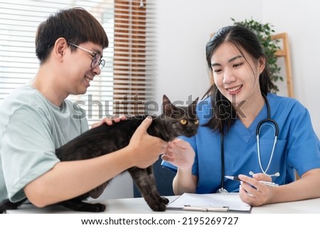 Veterinarian woman in blue uniform checks the health of pet appointment on a metal table while she is writing data on clipboard and prescription in veterinary clinic.