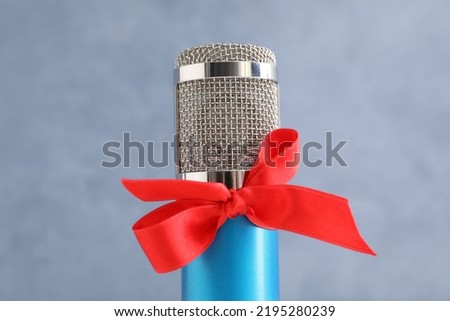 Microphone with red bow on grey background, closeup. Christmas music