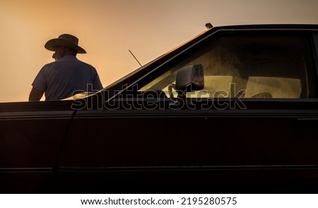 Portrait of adult man in cowboy hat standing against a vintage car during sunset