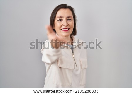 Middle age hispanic woman standing over isolated background smiling cheerful offering palm hand giving assistance and acceptance. 