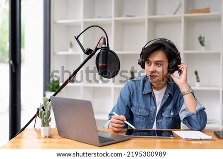 Asian man recording a podcast on laptop computer with microphone while online live streaming at home