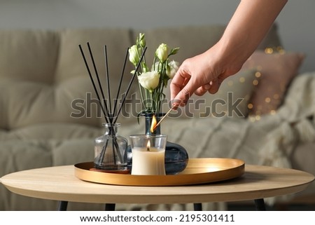 Woman lighting candle at wooden table in living room, closeup Royalty-Free Stock Photo #2195301411