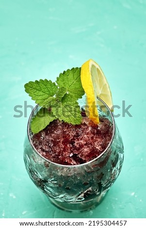 frozen red wine in a glass glass decorated with a slice of lemon and lemon leaves on a green background copy space. High quality photo