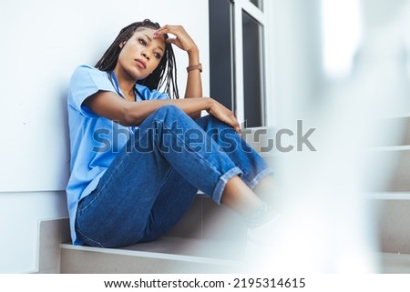 Upset female nurse standing in hospital corridor. Medical professional looking unhappy. Shot of a young nurse looking stressed out while sitting at a window in a hospital. Upset female nurse