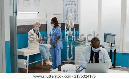 Female nurse and senior patient with face mask doing checkup visit in medical cabinet, consulting woman with sickness. Health assistant giving support and advice with healthcare treatment.