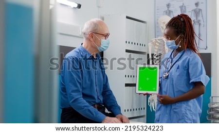 Assistant showing tablet with greenscreen to senior patient during covid 19 pandemic. Looking at isolated mockup template with blank copyspace and chromakey display at checkup visit.