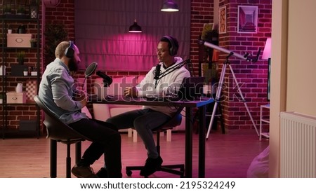 African american podcaster greeting guest doing fist bump hand gesture while recording podcast using digital video camera in home studio. Internet radio host in interview with famous influencer.