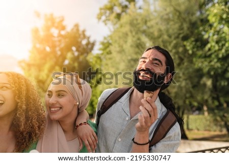 Multiracial friends eating ice cream in the park and having fun, focus on bearded man.