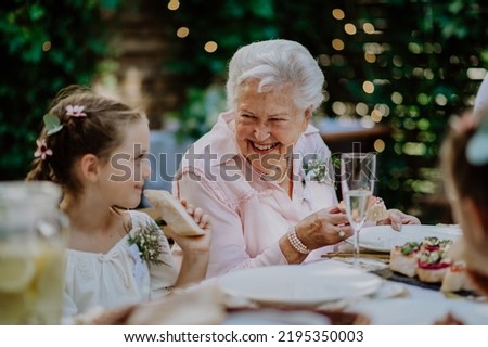 Wedding guests sitting by table, eating and drinking at reception outside in the backyard. Royalty-Free Stock Photo #2195350003