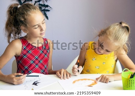 selective focus on two Cute schoolgirls, they are sitting at a table and drawing Halloween symbols on paper with pencils, making decorations for the holiday