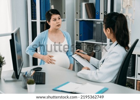 Korean expectant mom is listening attentively to her gynecologist doctor as she is giving consultation with a clipboard at desk in the hospital office. Royalty-Free Stock Photo #2195362749